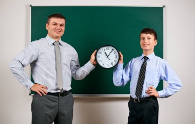 Bir adam ve çocuk kara tahta arka plan yakınında bir iş elbisesi giymiş portresi, onlar saat göstermek - öğrenme ve eğitim kavramı