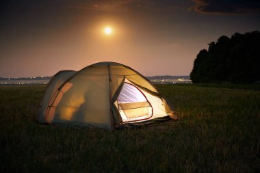 Seyahat ve kamp konsepti - yıldız dolu bir gökyüzü altında geceleri kamp çadırı. Turuncu ışıklı çadır içinde bir kişi ile. Güzel doğa - alan, orman, düz. Ay ve ay ışığı