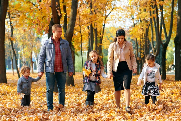 Mutlu aile sonbahar şehir parkında tatil yapıyor. Çocuklar ve ebeveynler poz veriyor, gülümsüyor, oynuyor ve eğleniyorlar. Parlak sarı ağaçlar ve yapraklar — Stok fotoğraf