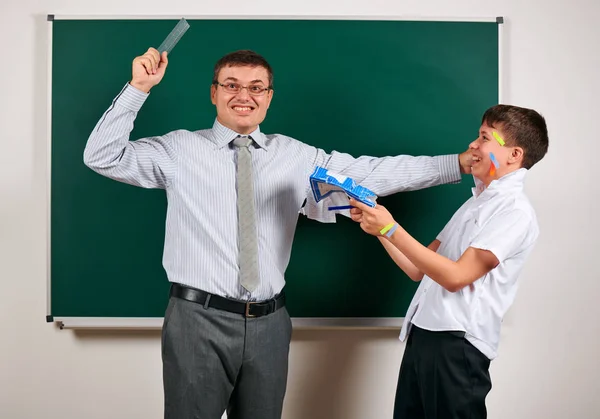 Portrait of a teacher catch the ear funny schoolboy with low discipline. Pupil very emotional, having fun and very happy, posing at blackboard background - back to school and education concept — Stock Photo, Image