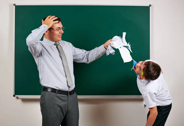 Portrait of a teacher and funny schoolboy with low discipline. Pupil very emotional, having fun and very happy, posing at blackboard background - back to school and education concept