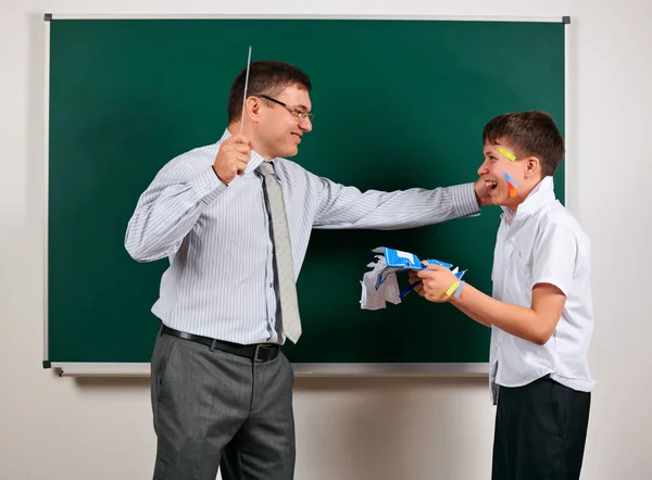 Portrait of a teacher catch the ear funny schoolboy with low discipline. Pupil very emotional, having fun and very happy, posing at blackboard background - back to school and education concept — Stock Photo, Image