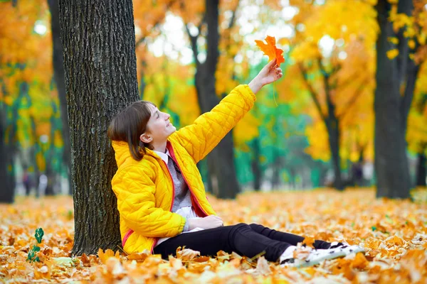 Teen girl seduta con foglie autunnali nel parco cittadino, ritratto all'aperto — Foto Stock