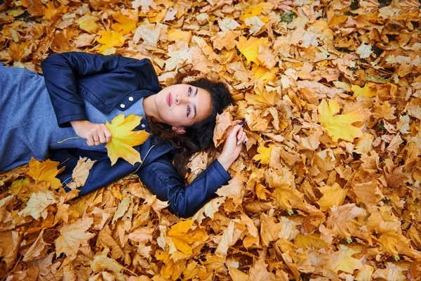 Woman lying with autumn leaves in city park, outdoor portrait — Stock Photo, Image
