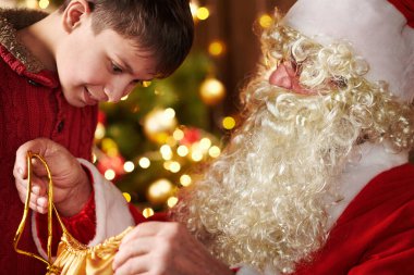 Noel Baba bir çanta açar ve çocuklara hediyeler verir, dekore edilmiş yılbaşı ağacının yanında oturur - Mutlu Noeller ve mutlu tatiller!