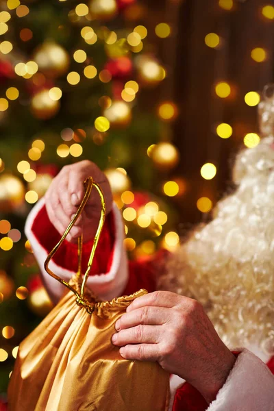 Père Noël ouvre un sac de cadeaux, assis à l'intérieur près de l'arbre de Noël décoré avec des lumières Joyeux Noël et Joyeuses Fêtes ! — Photo