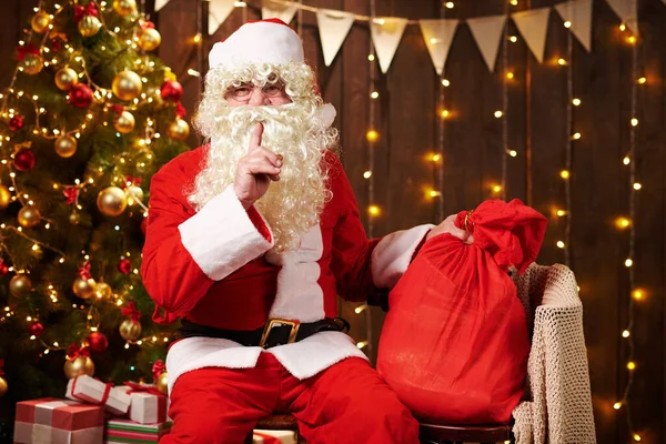 Père Noël posant avec un sac de cadeaux, assis à l'intérieur près décoré arbre de Noël avec des lumières Joyeux Noël et Joyeuses Fêtes ! — Photo
