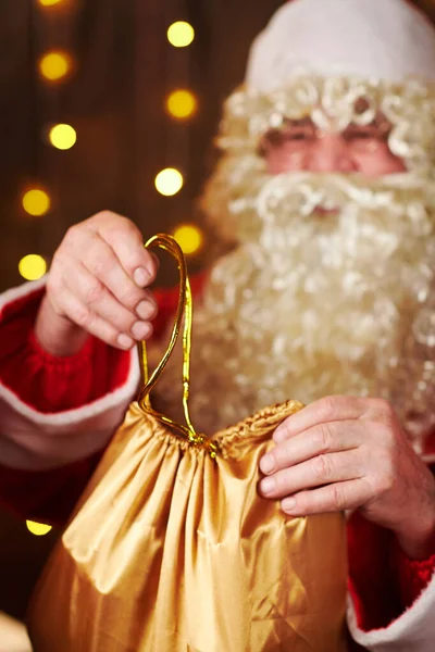 Père Noël ouvre un sac de cadeaux, assis à l'intérieur près de l'arbre de Noël décoré avec des lumières Joyeux Noël et Joyeuses Fêtes ! — Photo