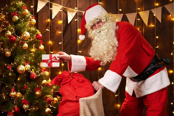 Père Noël posant avec sac de cadeaux à l'intérieur près de l'arbre de Noël décoré avec des lumières Joyeux Noël et Joyeuses Fêtes ! — Photo