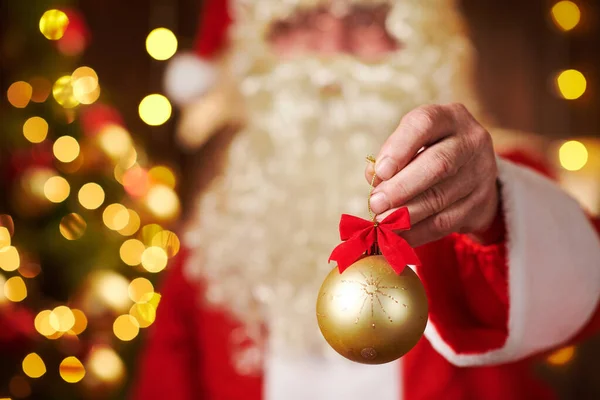 Gros plan des mains du Père Noël avec décoration de boule de Noël, assis à l'intérieur près de l'arbre de Noël décoré avec des lumières Joyeux Noël et Joyeuses Fêtes ! — Photo