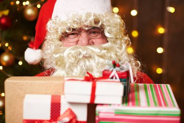 Noel Baba bir sürü hediyeyle poz veriyor, kapalı bir yerde süslü Noel ağacının yanında oturuyor - Mutlu Noeller ve mutlu tatiller!