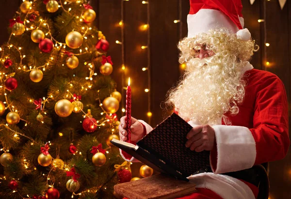 Libro di lettura di Babbo Natale, seduto al coperto vicino all'albero di Natale decorato con luci Buon Natale e Buone Feste ! — Foto Stock