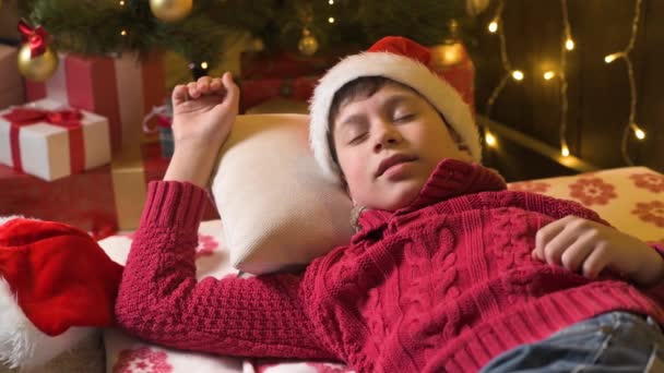 圣诞老人的助手男孩正在睡觉 等待圣诞老人的到来 他躺在装饰过的圣诞树旁 点着灯 圣诞快乐 节日快乐 — 图库视频影像