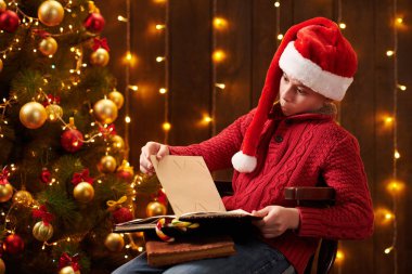 Genç çocuk kitap okuyor, kapalı bir yerde Noel Baba yardımcısı gibi giyinmiş, ışıklarla süslenmiş Xmas ağacının yanında oturuyor.!