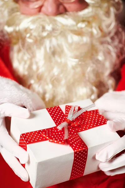 Primo piano delle mani di Babbo Natale con confezione regalo, seduto vicino all'albero di Natale decorato con luci Buon Natale e Buone Feste ! — Foto Stock
