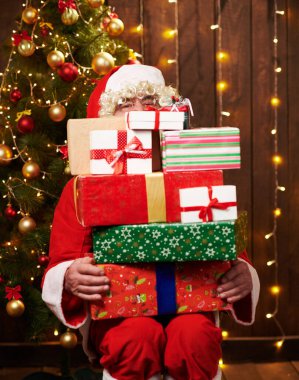 Noel Baba bir sürü hediyeyle poz veriyor, kapalı bir yerde süslü Noel ağacının yanında oturuyor - Mutlu Noeller ve mutlu tatiller!