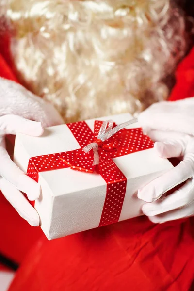 Primo piano delle mani di Babbo Natale con confezione regalo, seduto vicino all'albero di Natale decorato con luci Buon Natale e Buone Feste ! — Foto Stock