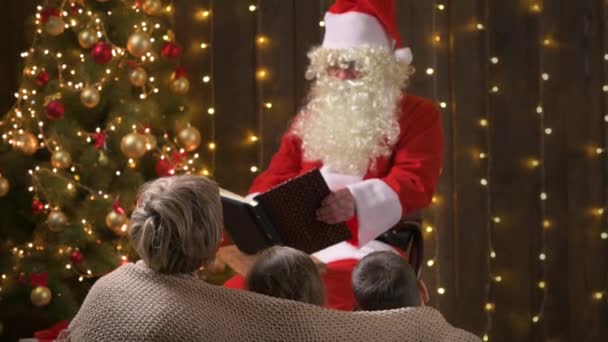 圣诞老人在为家人读书 母亲和孩子们坐在装饰过的圣诞树旁 点着灯听着 圣诞快乐和节日快乐 — 图库视频影像