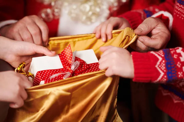 Babbo Natale apre una borsa e fa regali ai bambini, seduti vicino all'albero di Natale decorato con luci Buon Natale e Buone Feste ! — Foto Stock