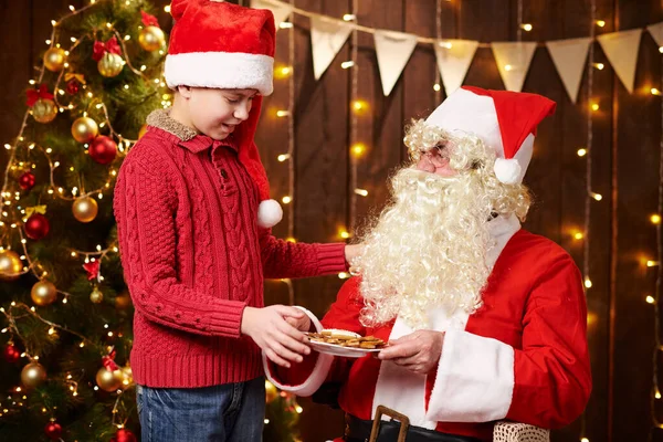 Санта Клаус і хлопчик п "ють чай, їдять печиво, розмовляють і сидять у приміщенні біля прикрашеного ксами дерева з вогнями - Веселого Різдва і Веселих свят.! — стокове фото