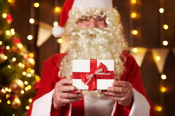 Gros plan des mains du Père Noël avec boîte cadeau, assis à l'intérieur près de l'arbre de Noël décoré avec des lumières Joyeux Noël et Joyeuses Fêtes ! — Photo