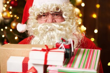 Noel Baba bir sürü hediyeyle poz veriyor, kapalı bir yerde süslü Noel ağacının yanında oturuyor - Mutlu Noeller ve mutlu tatiller!