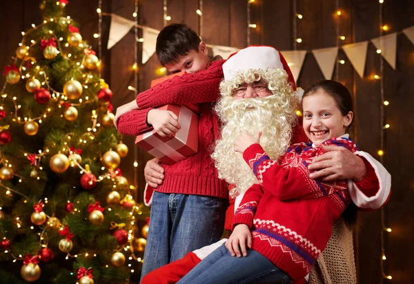 Санта Клаус і хлопчик і дівчинка, що тиняються в приміщенні біля прикрашеного дерева ксам зі світлом, вони розмовляють, усміхаються і приймають подарунки - Веселого Різдва і Веселих свят.! — стокове фото