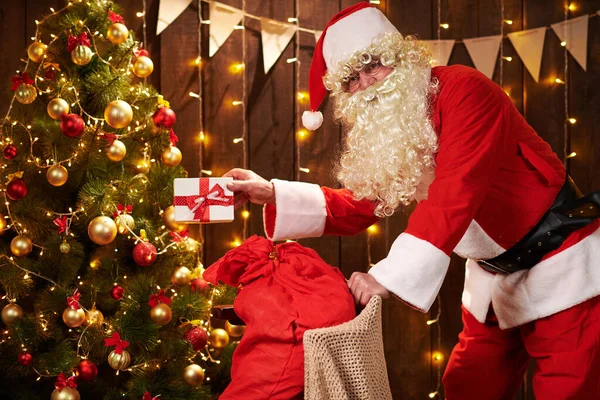 Père Noël posant avec sac de cadeaux à l'intérieur près de l'arbre de Noël décoré avec des lumières Joyeux Noël et Joyeuses Fêtes ! — Photo