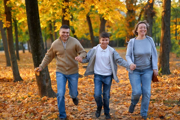 Šťastnou rodinnou dovolenou v podzimním městském parku. Děti a rodiče běží, usmívají se, hrají si a baví se. Jasně žluté stromy a listy — Stock fotografie