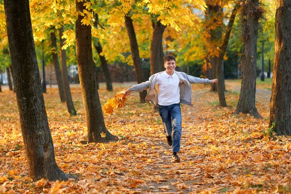 Boy teenager having holiday in autumn city park, running, smiling, playing and having fun. Bright yellow trees and leaves — Stok fotoğraf
