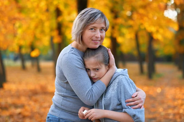 Retrato de la madre con su triste hija en el parque de otoño de la ciudad. Árboles y hojas de color amarillo brillante — Foto de Stock