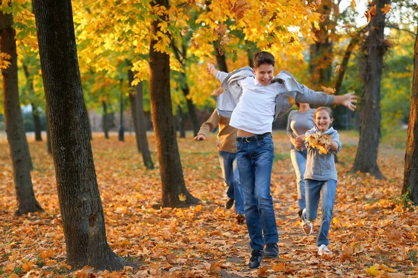 Mutlu aile sonbahar şehir parkında tatil yapıyor. Çocuklar ve ebeveynler koşuyor, gülümsüyor, oynuyor ve eğleniyorlar. Parlak sarı ağaçlar ve yapraklar — Stok fotoğraf