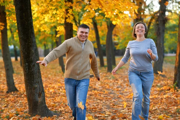 Mutlu çift sonbahar şehir parkında tatil yapıyor. Erkek ve kadın koşuyor, gülümsüyor, oynuyor ve eğleniyorlar. Parlak sarı ağaçlar ve yapraklar — Stok fotoğraf