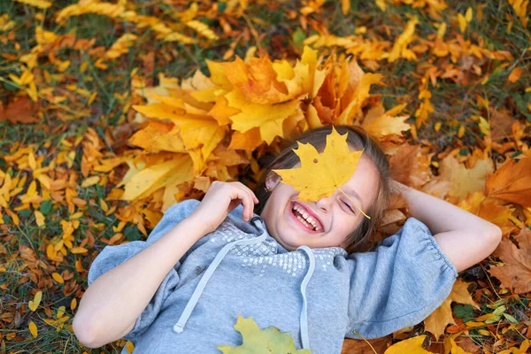 Ragazza in vacanza nel parco cittadino autunnale, sdraiata sull'erba, in posa, sorridente, giocando e divertendosi. Luminosi alberi e foglie gialle — Foto Stock