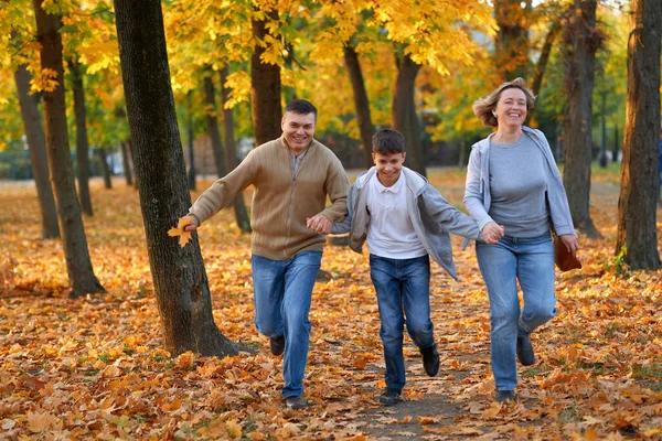 Mutlu aile sonbahar şehir parkında tatil yapıyor. Çocuklar ve ebeveynler koşuyor, gülümsüyor, oynuyor ve eğleniyorlar. Parlak sarı ağaçlar ve yapraklar — Stok fotoğraf