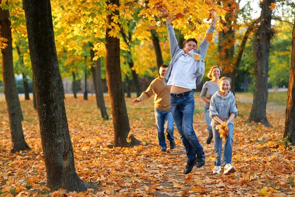 Szczęśliwy rodzina mający święto w jesienny miejski park. Dzieci i rodzice biegają, uśmiechają się, bawią i bawią. Jasnożółte drzewa i liście — Zdjęcie stockowe
