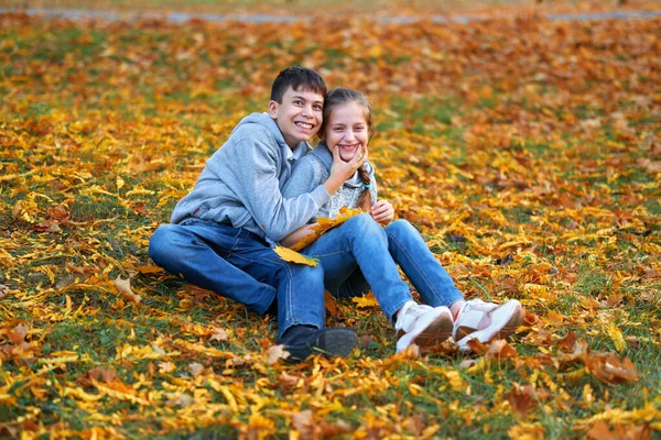 Dívka a chlapec teenager mají dovolenou v podzimním městském parku, pózování, usmívání, hraní a baví. Jasně žluté stromy a listy — Stock fotografie