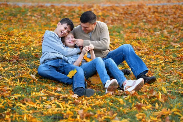 Szczęśliwy rodzina mający święto w jesienny miejski park. Dzieci i rodzice pozowanie, uśmiech, zabawy i zabawy. Jasnożółte drzewa i liście — Zdjęcie stockowe