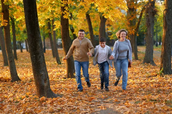 Mutlu aile sonbahar şehir parkında tatil yapıyor. Çocuklar ve ebeveynler koşuyor, gülümsüyor, oynuyor ve eğleniyorlar. Parlak sarı ağaçlar ve yapraklar — Stok fotoğraf