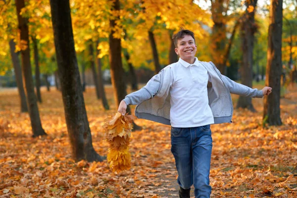 Boy teenager having holiday in autumn city park, running, smiling, playing and having fun. Bright yellow trees and leaves — Zdjęcie stockowe