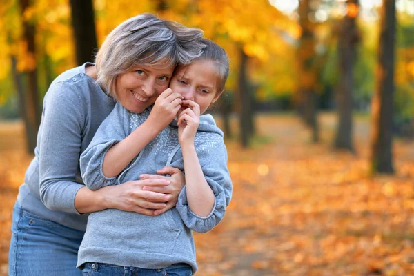 Ritratto di madre con la sua triste figlia nel parco cittadino autunnale. Luminosi alberi e foglie gialle — Foto Stock