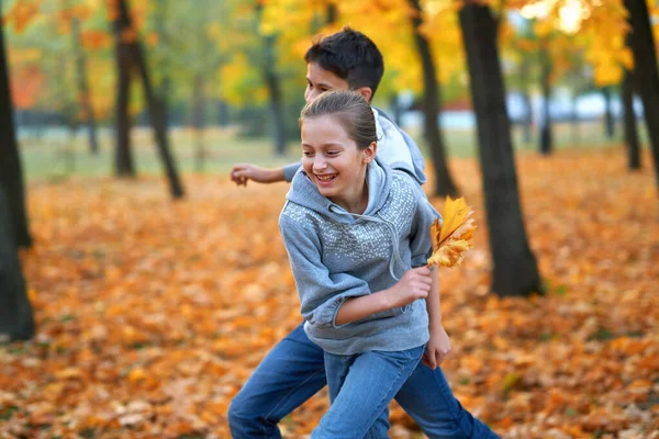 Flicka och pojke tonåring som semestrar i höstens stadspark, springer, ler, leker och har roligt. Ljusgula träd och blad — Stockfoto