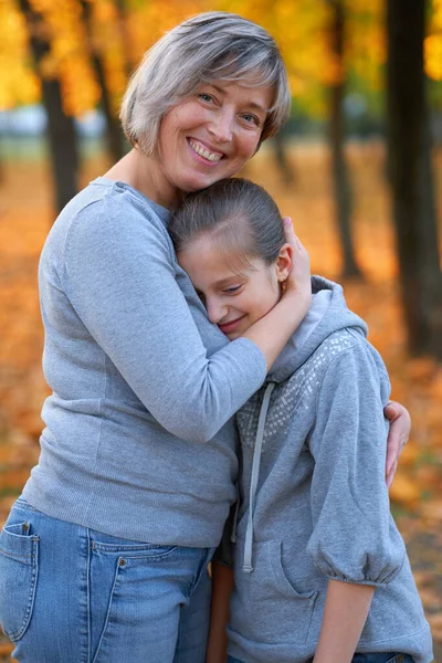 Ritratto di madre con la sua triste figlia nel parco cittadino autunnale. Luminosi alberi e foglie gialle — Foto Stock