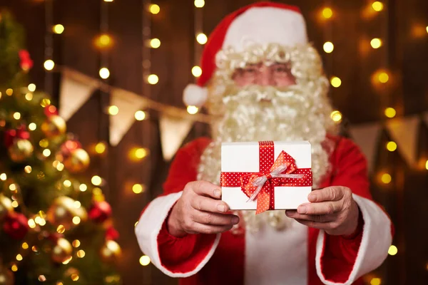 Primo piano delle mani di Babbo Natale con confezione regalo, seduto vicino all'albero di Natale decorato con luci Buon Natale e Buone Feste ! — Foto Stock