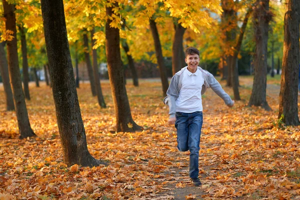 Boy teenager having holiday in autumn city park, running, smiling, playing and having fun. Bright yellow trees and leaves — Zdjęcie stockowe