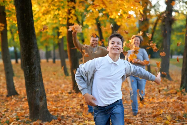 Mutlu aile sonbahar şehir parkında tatil yapıyor. Çocuklar ve ebeveynler koşuyor, gülümsüyor, oynuyor ve eğleniyorlar. Parlak sarı ağaçlar ve yapraklar — Stok fotoğraf