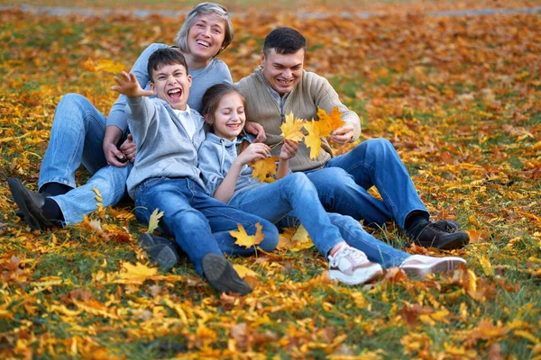 Glad familj som har semester i höstens stadspark. Barn och föräldrar poserar, ler, leker och har roligt. Ljusgula träd och blad — Stockfoto