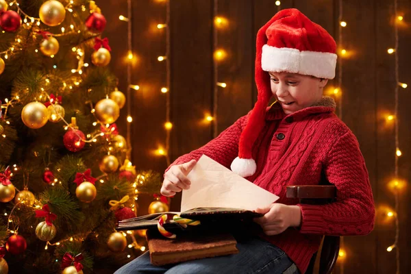 Підліток читає книжку "Веселого Різдва і щасливих свят", сидячи в приміщенні біля прикрашеного дерева ксам.! — стокове фото