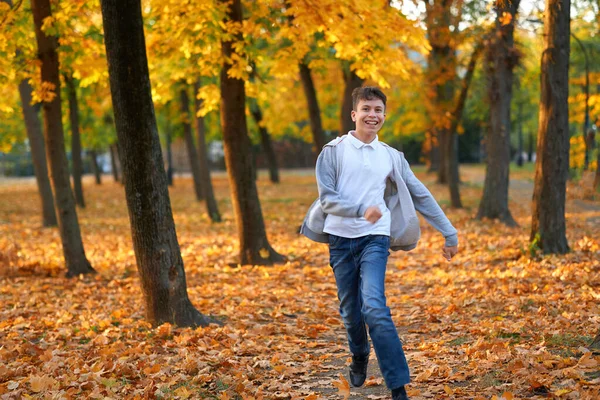 Menino adolescente tendo férias no parque da cidade de outono, correndo, sorrindo, jogando e se divertindo. Árvores e folhas amarelas brilhantes — Fotografia de Stock