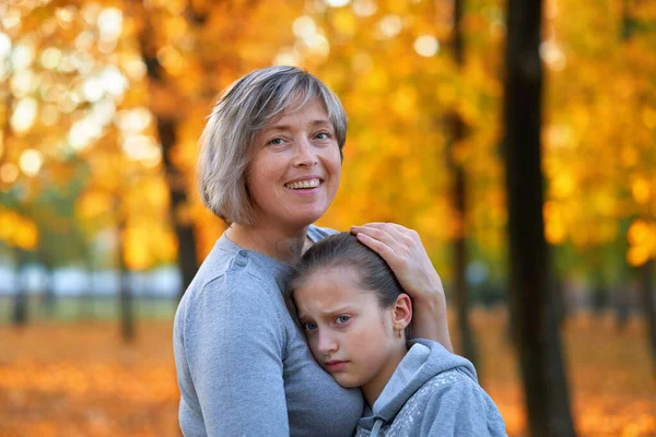 Portrét matky se svou smutnou dcerou v podzimním městském parku. Jasně žluté stromy a listy — Stock fotografie